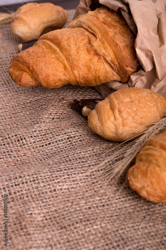 Croissants with chocolate on board near wheat on sackcloth background. Rustic style.