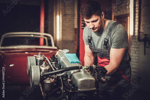 Mechanic working on classic car engine in restoration workshop