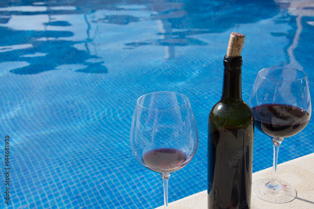 A bottle of red wine by the pool. Day, water and glass A bottle of red wine by the pool. Day, water and glass