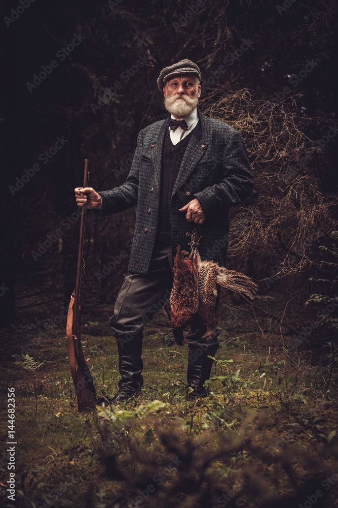 Senior hunter with a shotgun and pheasants in a traditional shooting clothing Senior hunter with a shotgun and pheasants in a traditional shooting clothing