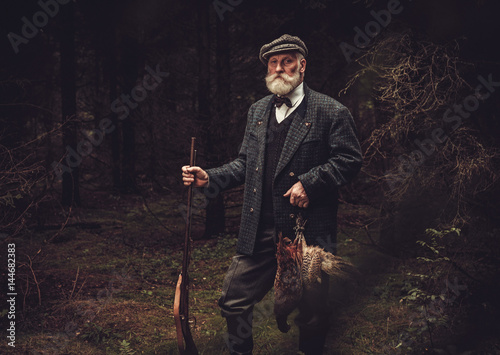 Senior hunter with a shotgun and pheasants in a traditional shooting clothing