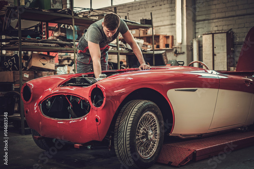 Mechanic working on classic car electrics in restoration workshop