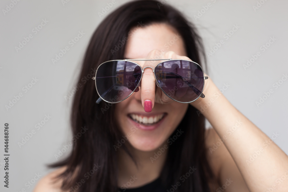 A beautiful girl trying on sunglasses. She's having fun and fooling around. Pointing finger, like a huge nose A beautiful girl trying on sunglasses. She's having fun and fooling around. Pointing finger, like a huge nose