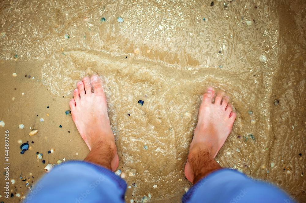 Fototapeta premium Feet on the beach in the sea and sand. Top view
