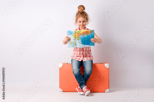 Child blonde girl with pink vintage suitcase and city map ready for summer vacation. Travel and adventure concept