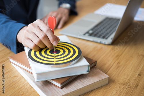 Foto Business Man hand holding a target with darts hitting the center