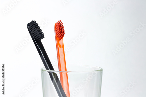 Closeup of two toothbrushes in a glass beaker. For men and women. Full black and orange brush. Brush for the family. Isolated on a white background