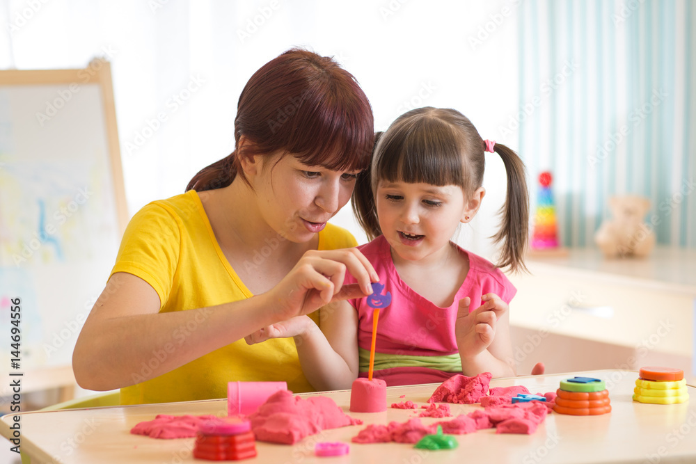 Fototapeta premium Śliczna mała dziewczynka i matka bawić się piaskiem kinetycznym w domu