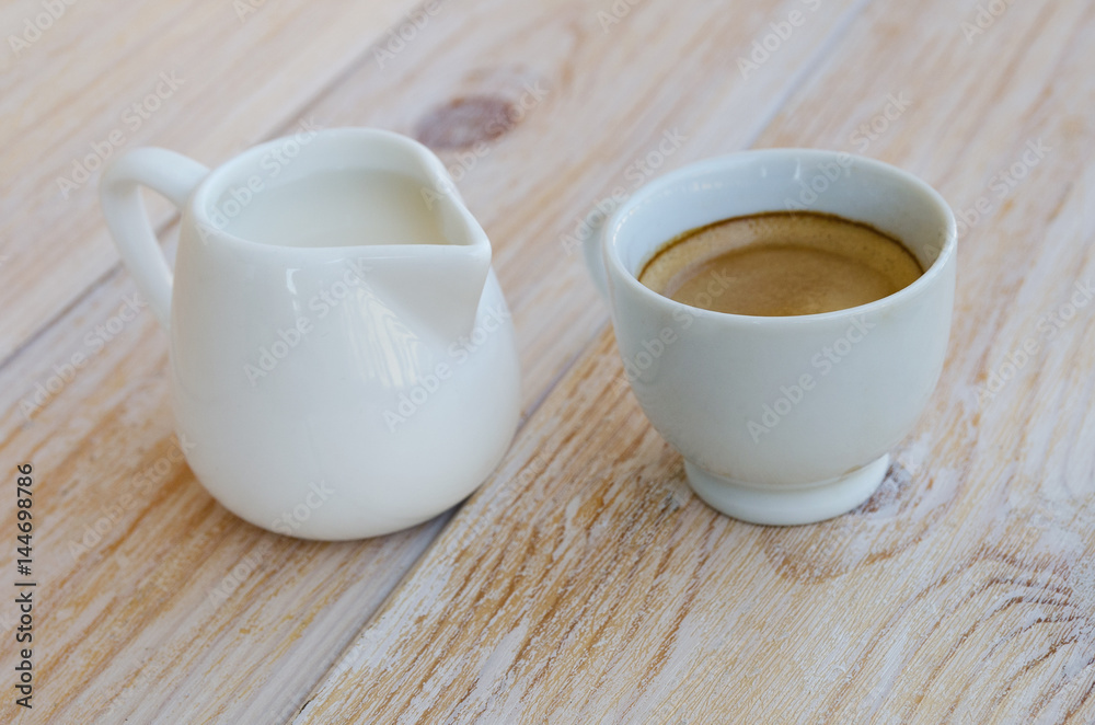 White porcelain cup of espresso and small milk jug on rustic wood table.  Black coffee with milk concept. Stock Photo | Adobe Stock