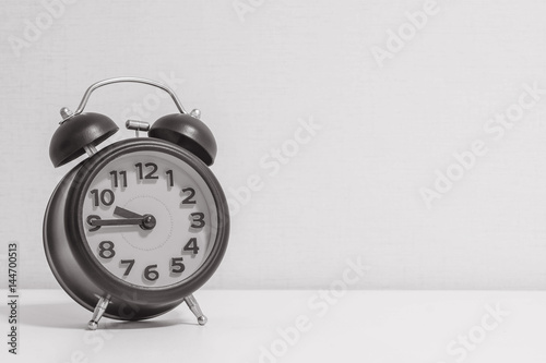 Closeup alarm clock for decorate show a quarter to ten o'clock or 9:45 a.m. on white wood desk and cream wallpaper textured background in black and white tone with copy space