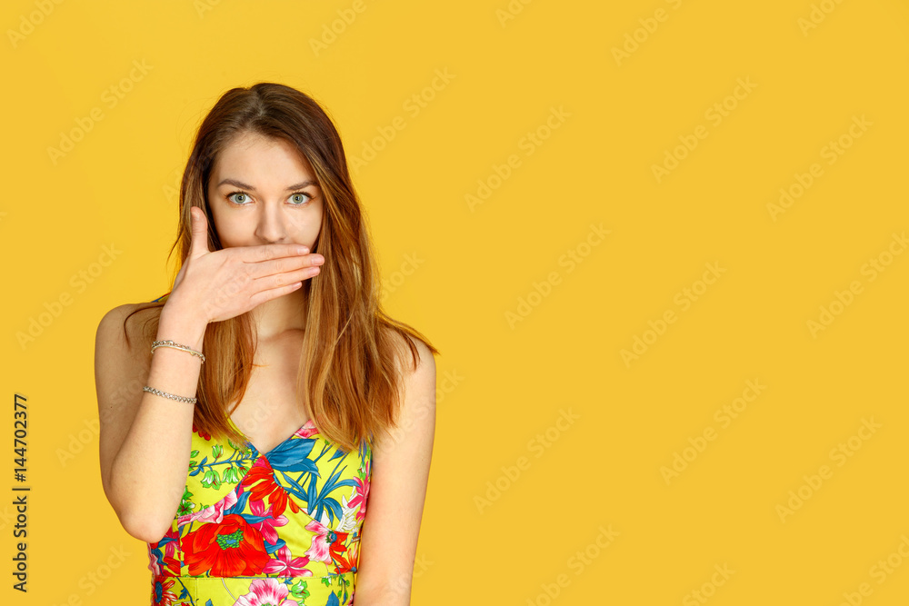 Beautiful girl against yellow wall, closes her mouth with her hand. Concept of female gossip Beautiful girl against yellow wall, closes her mouth with her hand. Concept of female gossip