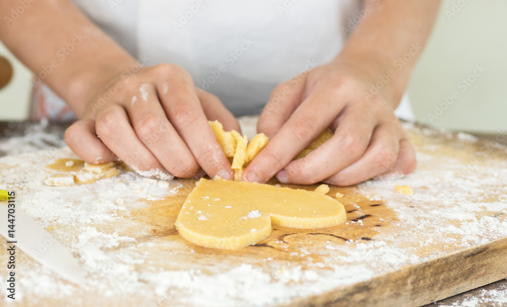 Hands cut heart shaped cookie from dough