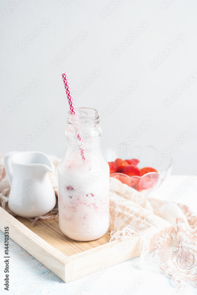 Healthy strawberry milkshake in glass bottle with ingredients on white table Healthy strawberry milkshake in glass bottle with ingredients on white table