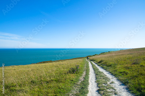 Couple walking on a hiking trail by a green field near the sea