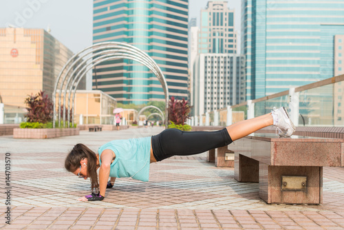 Fitness woman doing feet elevated push-ups on a bench in the city. Sporty girl exercising outdoors photo