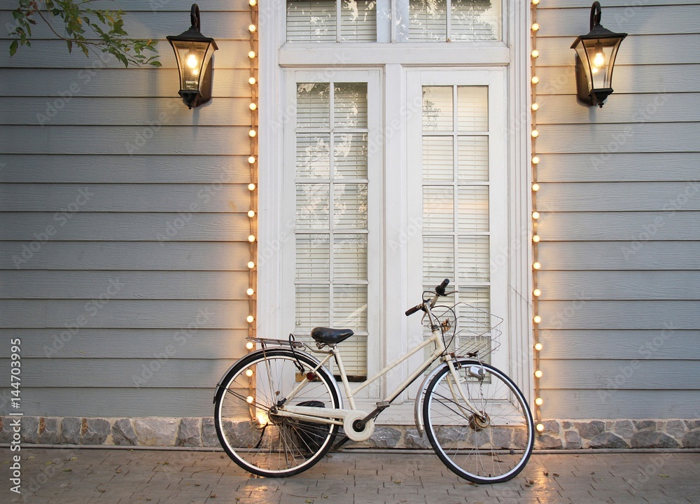 Vintage Bicycle lay on Classic style house entrance (grey walls, white wooden door and windows decorates with illuminate)