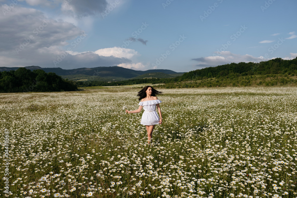 Young beautiful woman in a white dress enjoying chamomile field among mountains. Young beautiful woman in a white dress enjoying chamomile field among mountains.