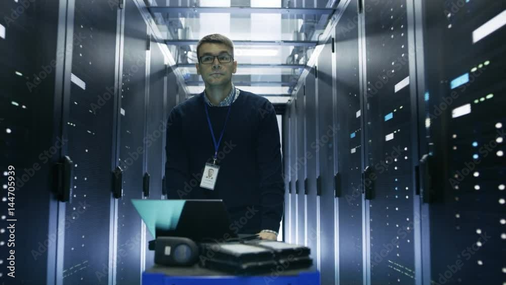 Following Shot of Server Engineer Pushing Crash Cart with Laptop, Hard Drives and Hardware Through Data Center. He Walks along Rows of Server Racks.  Shot on RED EPIC-W 8K Helium Cinema Camera.