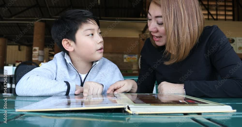 Asian cute boy with mother reading menu book and point .Happy face Asian cute boy with mother reading menu book and point .Happy face