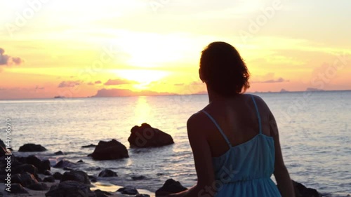 Happy young woman in a long dress dancing on the beach on a colourful sunset background
