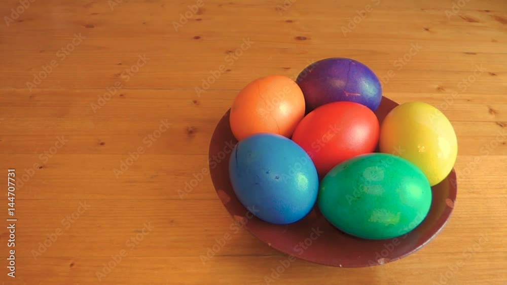 Colorful easter eggs is put on the table, and more eggs added later. Bright decoration elements on old ceramic plate on wooden surface. Traditional spring holiday theme. With place for text.
