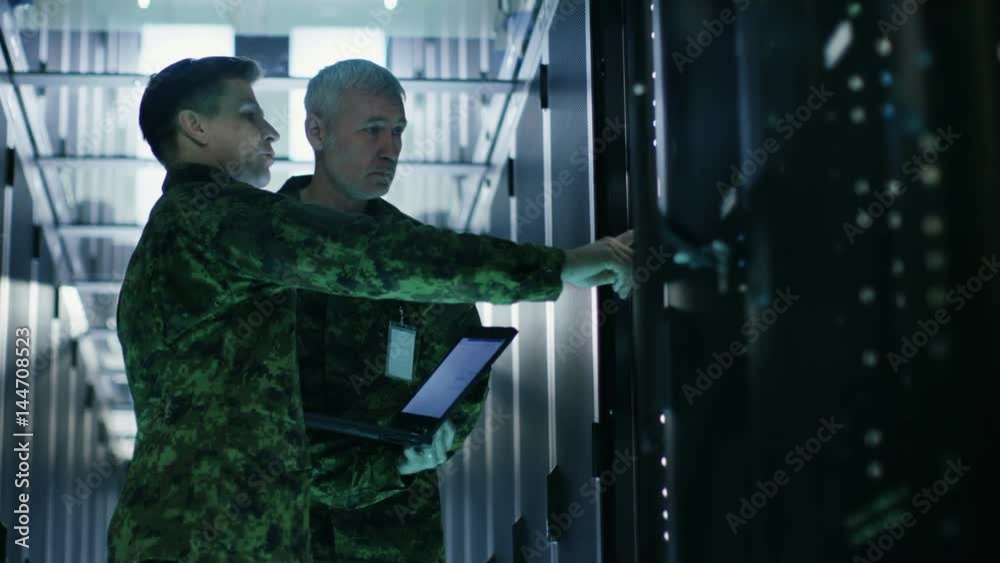In Data Center Two Military Men Work with Open Server Rack Cabinet. One Holds Military Edition Laptop. Shot on RED EPIC-W 8K Helium Cinema Camera. In Data Center Two Military Men Work with Open Server Rack Cabinet. One Holds Military Edition Laptop. Shot on RED EPIC-W 8K Helium Cinema Camera.