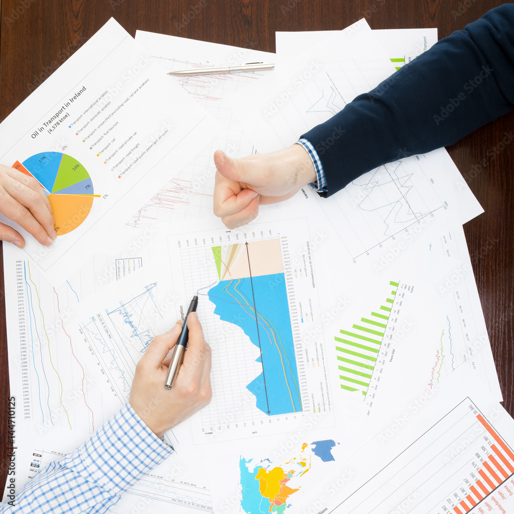 Banking, taxing and all things related with world of finance - two businessmen making agreement over a table with some financial data involved Banking, taxing and all things related with world of finance - two businessmen making agreement over a table with some financial data involved