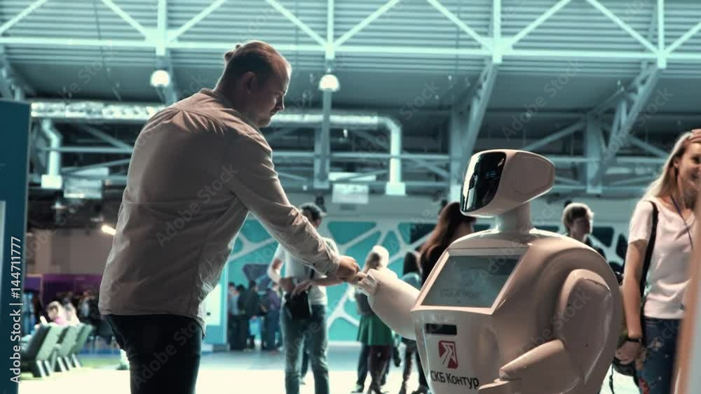 Modern Robotic Technologies. A man communicates with a robot, presses a plastic mechanical arm to the robot, handshake. Modern Robotic Technologies. A man communicates with a robot, presses a plastic mechanical arm to the robot, handshake.