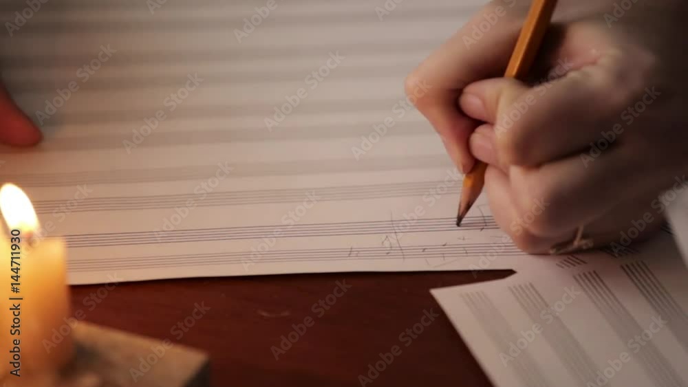 student writing a music: musician composing with a pencil in a music book with candlelight. close-up hand of musician student writing a music: musician composing with a pencil in a music book with candlelight. close-up hand of musician