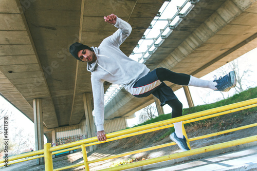 Young man training under the bridge, he jumping over the handrail.