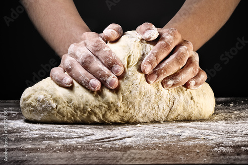 Woman's hands kneading the dough, on dark background.
