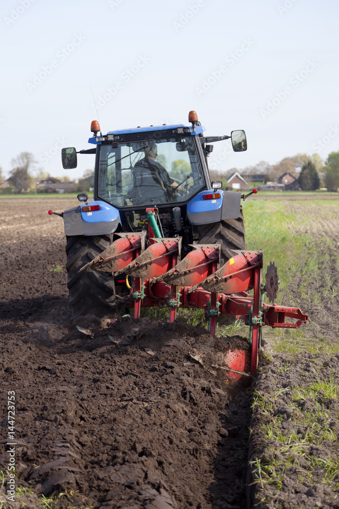 Obraz premium farmer ploughs filed with plough behind tractor near renswoude in the netherlands