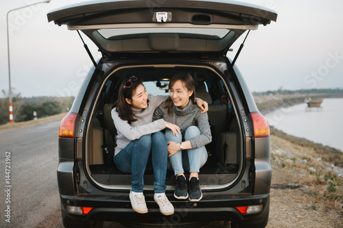 Canvas Print Two happy Asia woman friends enjoying road trip in hatchback car,flare light
