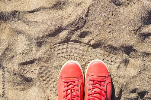 Concept with pink sneakers on bright sea sand. Summer vacation background with space for the text