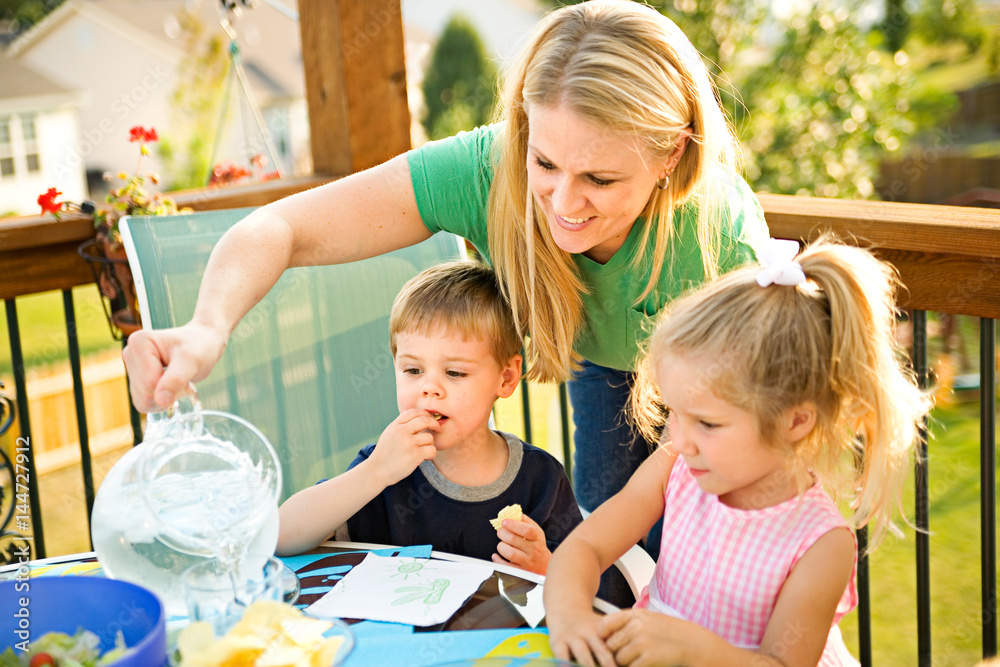 Fototapeta premium Dinner: Mother Pours Water Into Glasses For Children