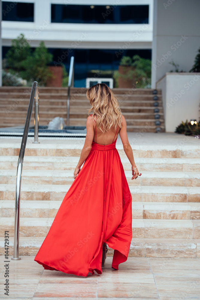 A girl with long curly hair in long red dress walking up the stairs ...