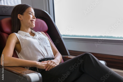 Happy commuter enjoying train travel to go to work in the morning. Asian woman enjoying view passing by relaxing in comfortable business class seat.