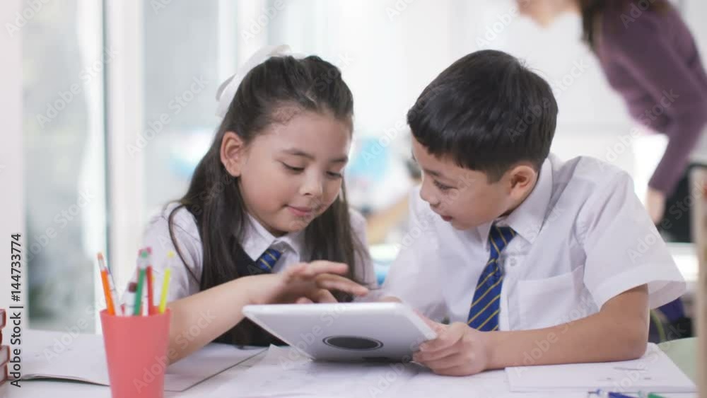 Happy little boy & girl working on computer tablet in school classroom Happy little boy & girl working on computer tablet in school classroom