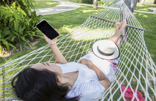 Asian woman relaxing in hammock using smartphone, Concept of vacation and relaxing
