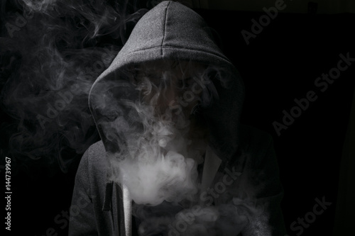 Tablou pe pânză vaping man wearing a hoody with lots of smoking clouds.