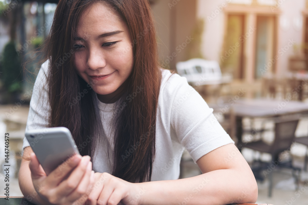 A beautiful Asian girl with smiley face holding and using smart phone in modern cafe