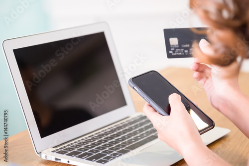 Online shopping concept. Selective focus of close up hands holding smartphone and credit card with laptop.