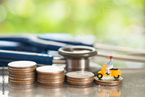Health and travel insurance, miniature people riding on coins stacks and stethoscope. Business, health care, and traveling concept.