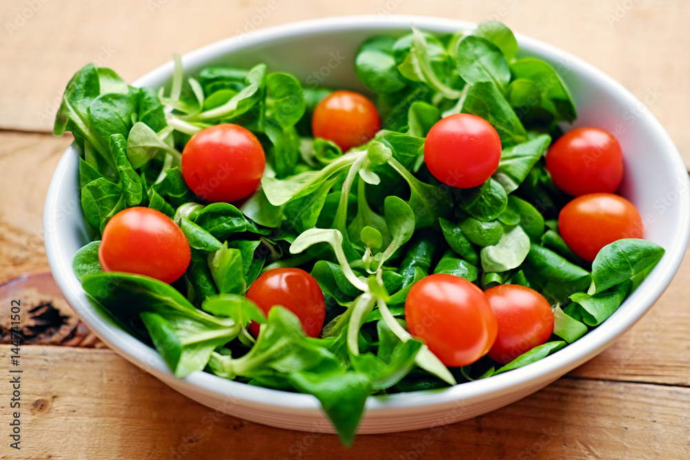 Cherry tomatoes and basil salad in a white cup on a wooden table. Cherry tomatoes and basil salad in a white cup on a wooden table.