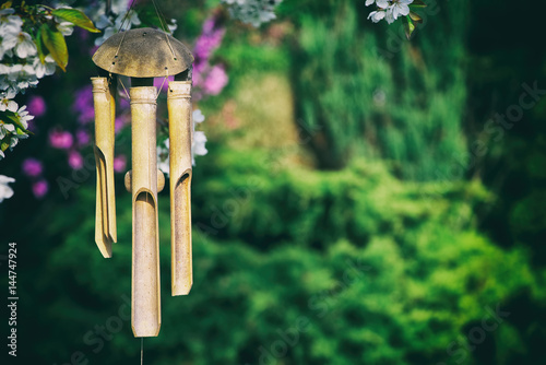 wind chimes hanging in a blooming tree, bamboo chimes in a garden 