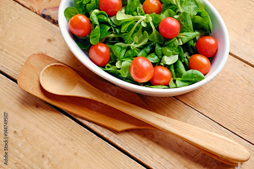 Cherry tomatoes and basil salad in a white cup on a wooden table.