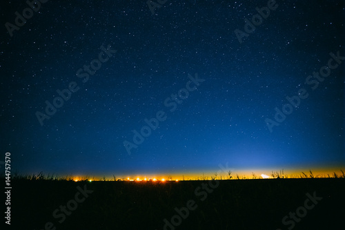 Night Starry Sky Above Field And Yellow City Lights On Background