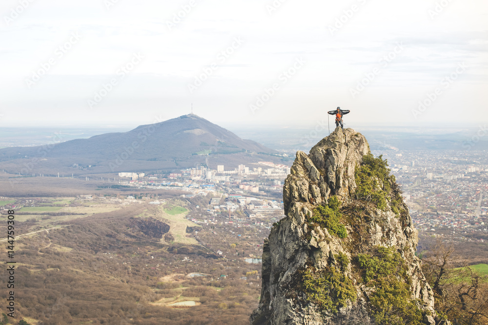 A young climber winds the rope to the tops of a steep cliff against the backdrop of the city and the caucasian mountain