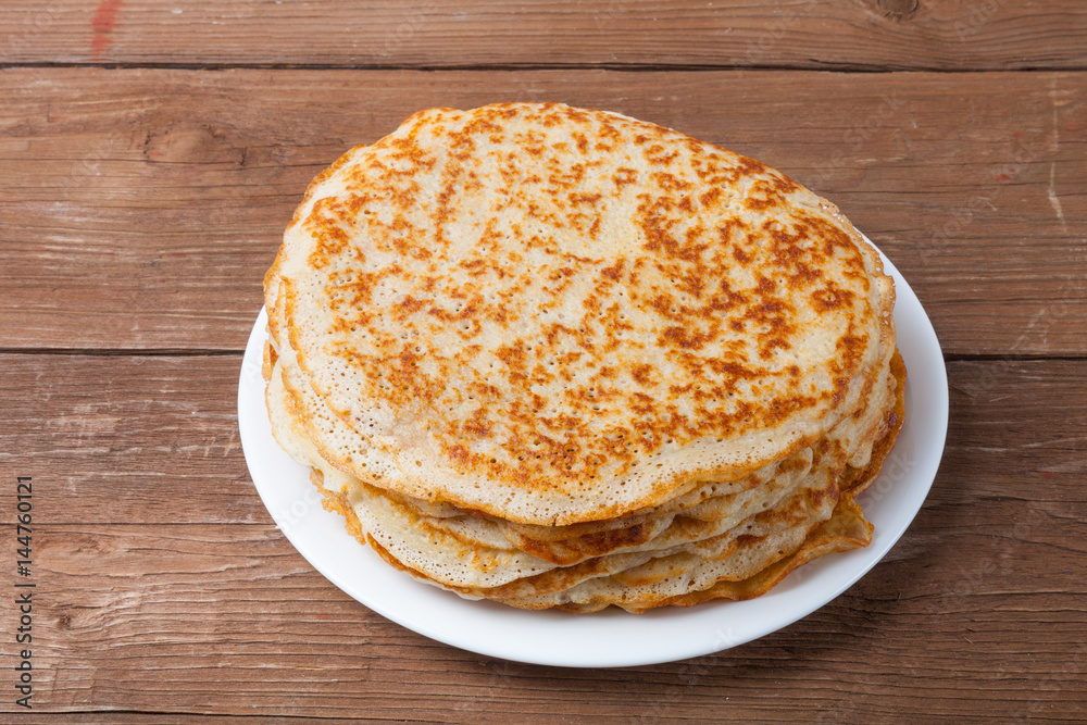 Stack of Russian pancakes - blini on a wite plate on old wooden table. Selective focus Stack of Russian pancakes - blini on a wite plate on old wooden table. Selective focus