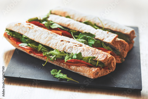 Healthy fresh crusty baguette submarine sandwich with salami, cheese and rucola. Selective focus